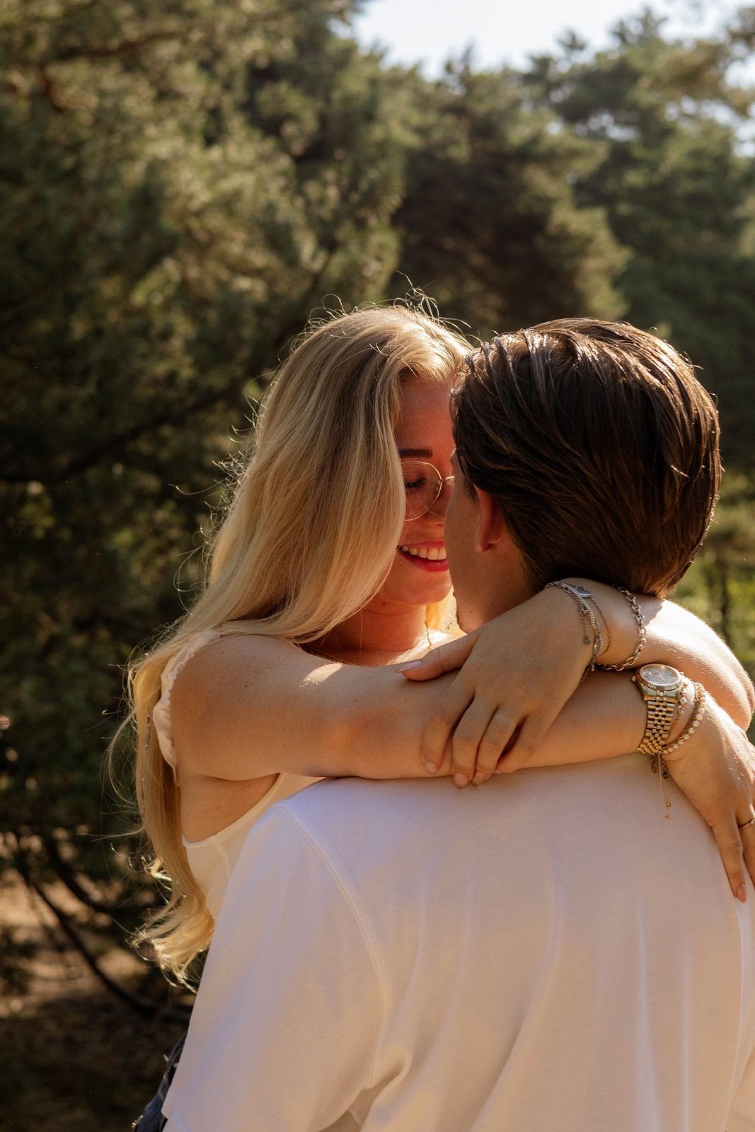 Vrouw met armen om haar partner, glimlachend in het bos