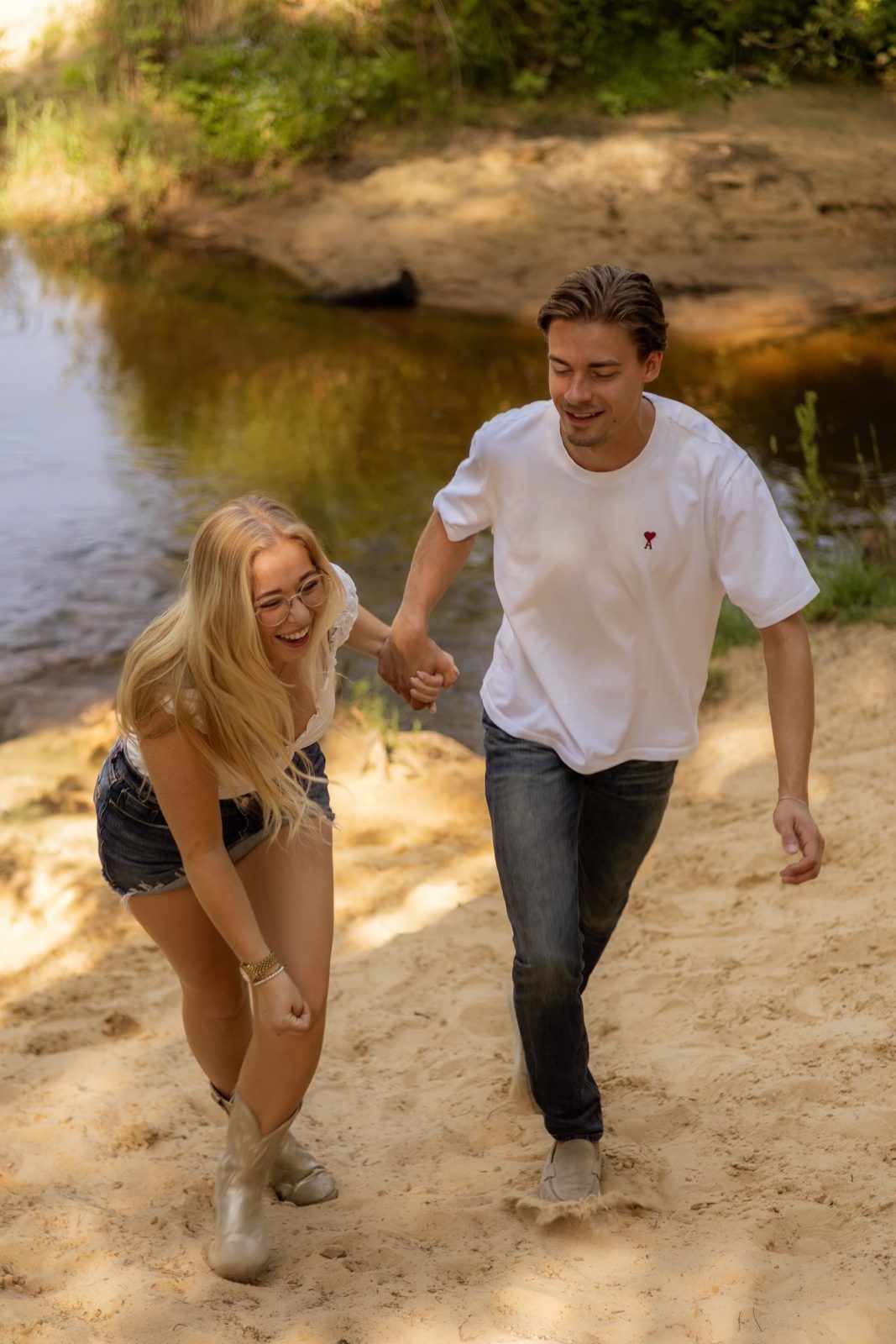 Lachend koppel loopt hand in hand over een zandpad bij het water